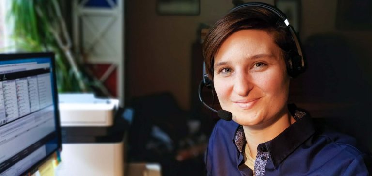 Jasmin Gajewski trägt ein Headset an einem Computer und lächelt in die Kamera