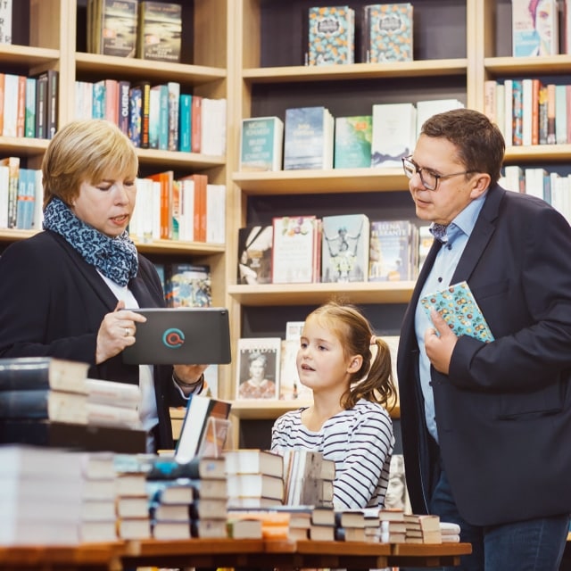 Buchhändlerin verwaltet einfach in der Buchhandlung direkt mit dem Kunden seine gewünschten Bestellungen. Das Kind sieht, wie einfach die Buchhändlerin über das Quimus System am Tablet die Bestellungen von ihrem Vater verwaltet.