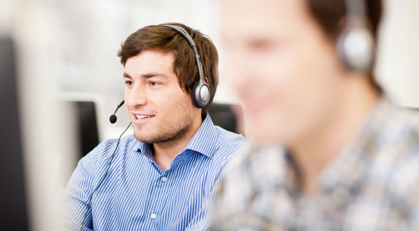 Ein Mann sitzt mit Headset vor einem Computer