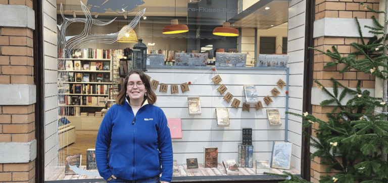 Eine Buchhändlerin steht vor dem Schaufenster ihres Geschäfts.