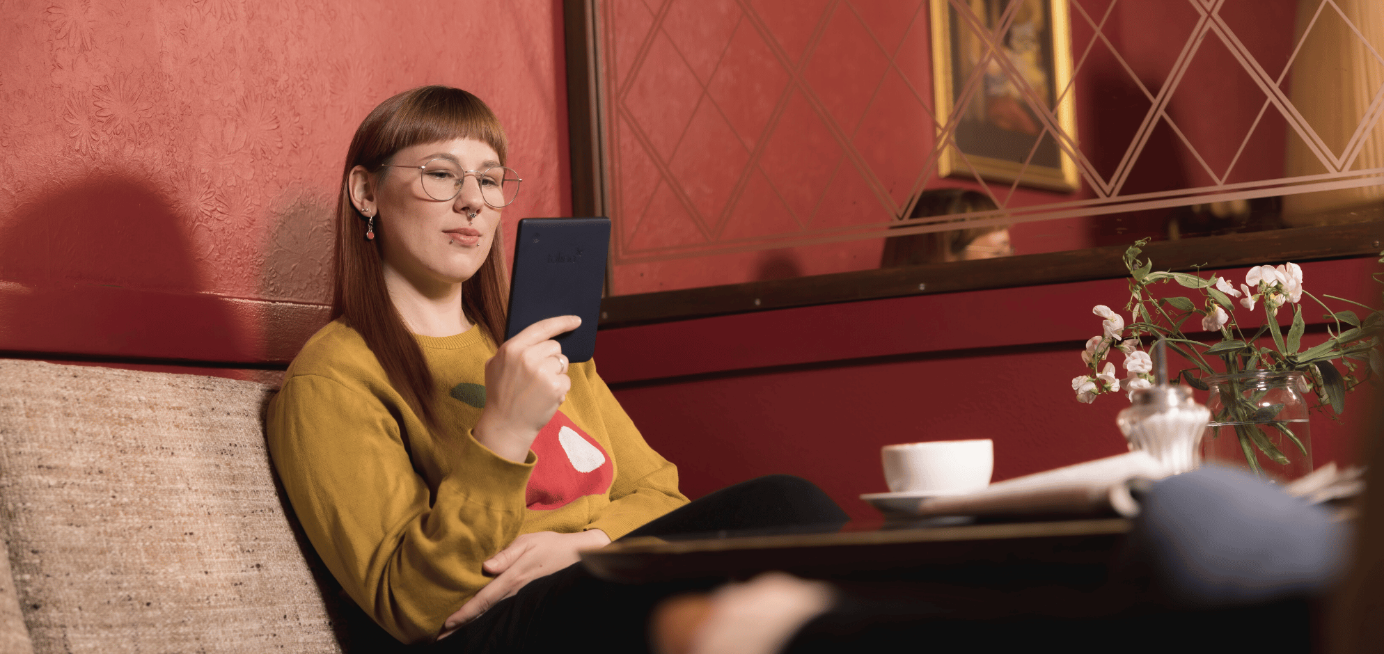 Eine junge Frau sitzt auf einem Sofa im Cafe und liest auf einem eReader.