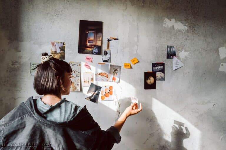 Eine Frau bringt Post-Its an einer grauen Wand mit Schattenwurf an.