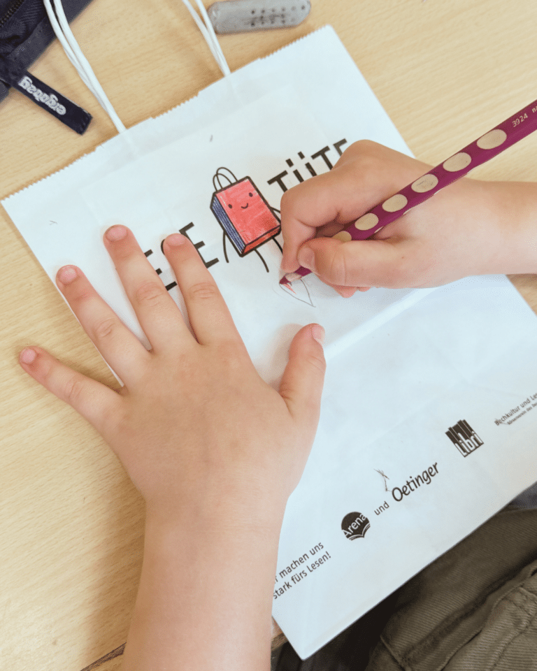 Kinderhände, die eine Lesetüte bemalen.