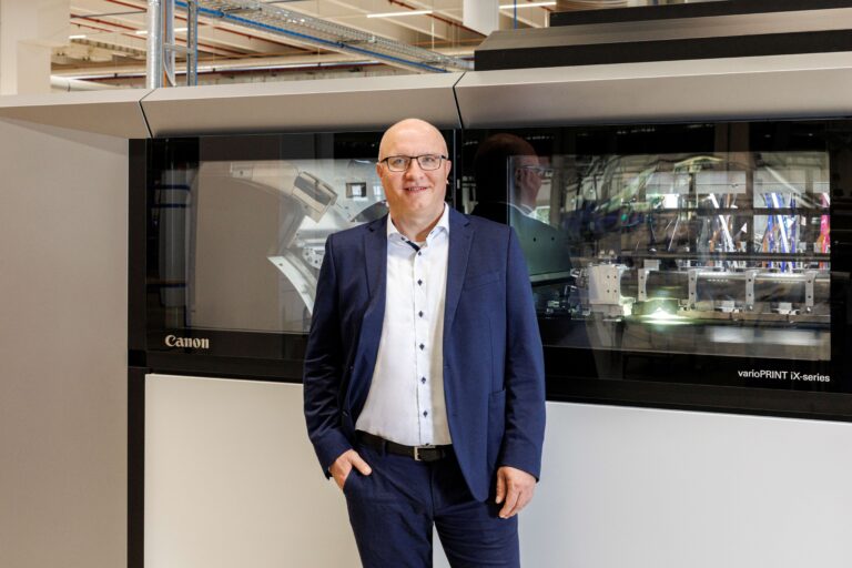 Geschäftsführer Ulrich Vollmer stehend vor dem Drucksystem Canon.
