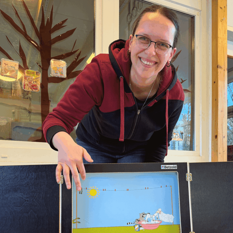 Vorlesetag 2025: Person, die in die Kamera lächelt und auf ein Kamishibai zeigt.